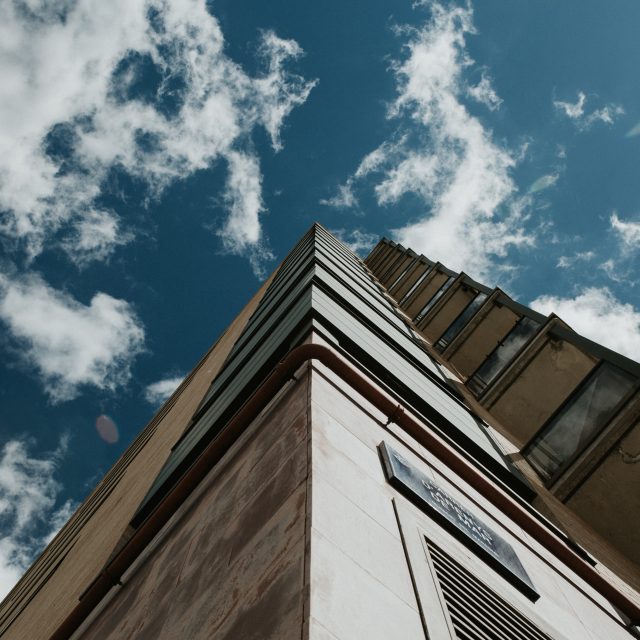 A low angle shot of a high-rise building under a clear blue sky with white clouds