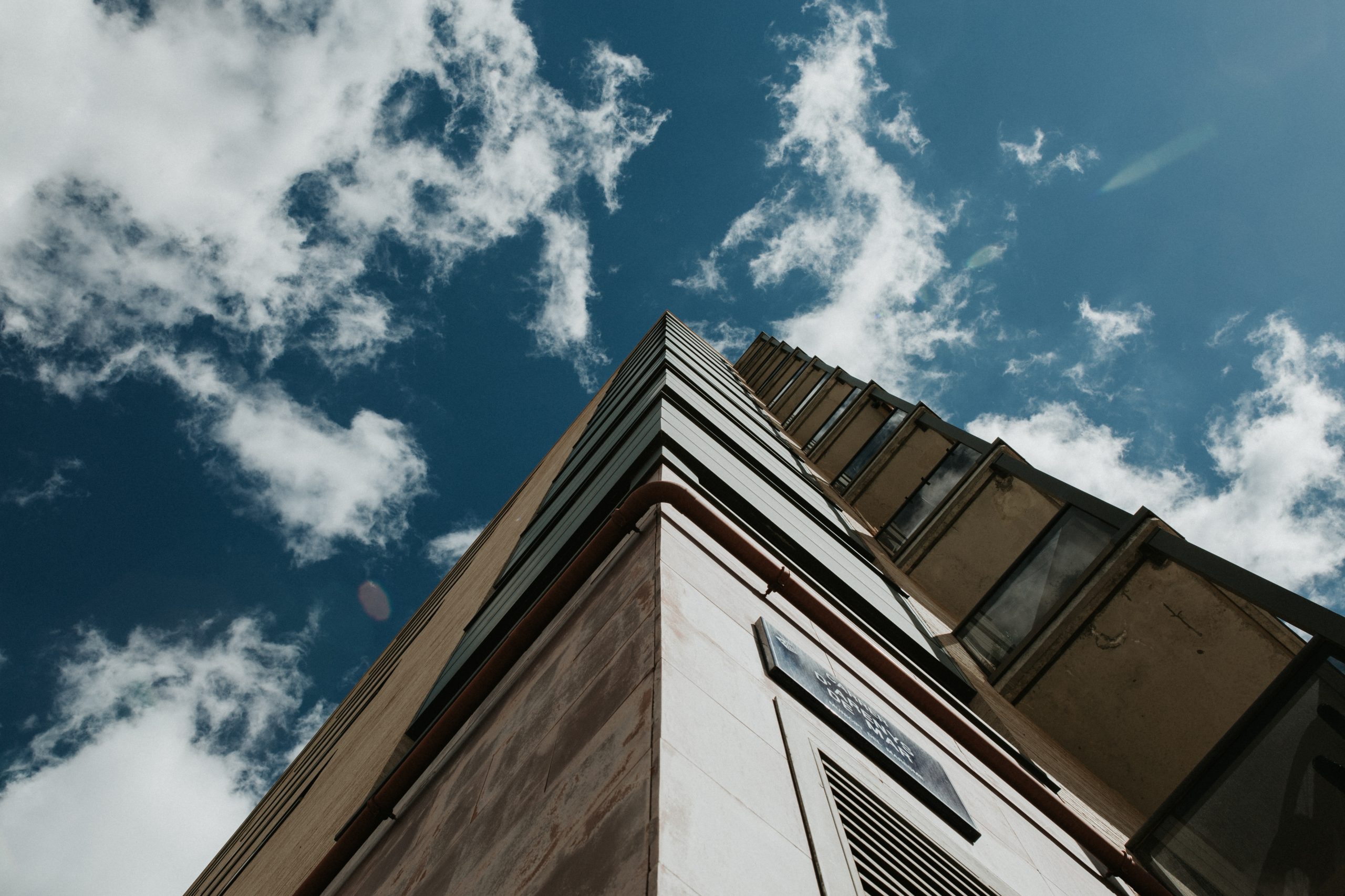 Low angle shot of a high-rise building under a clear blue sky with white clouds A low angle shot of a high-rise building under a clear blue sky with white clouds